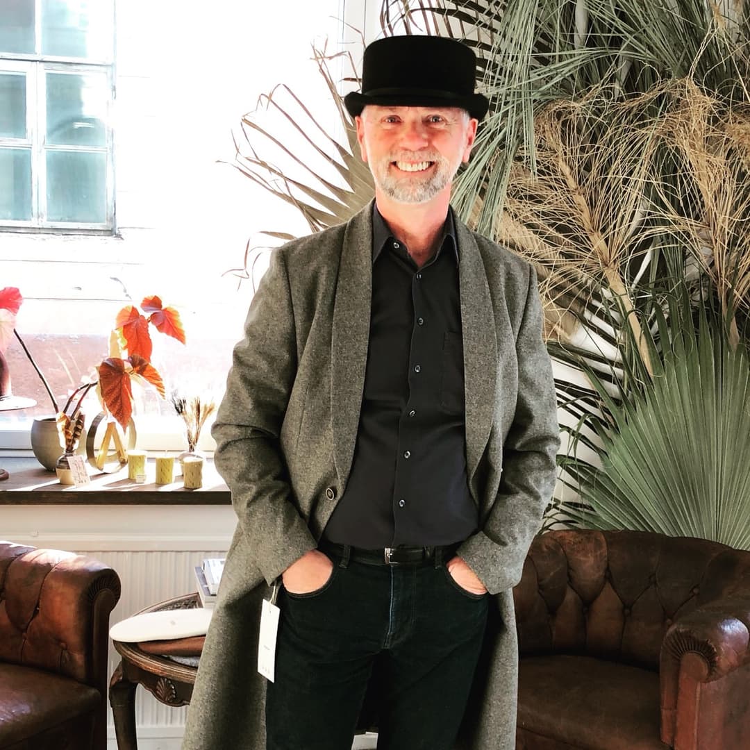 Paul Donders con sombrero negro y abrigo, sonriendo en un café