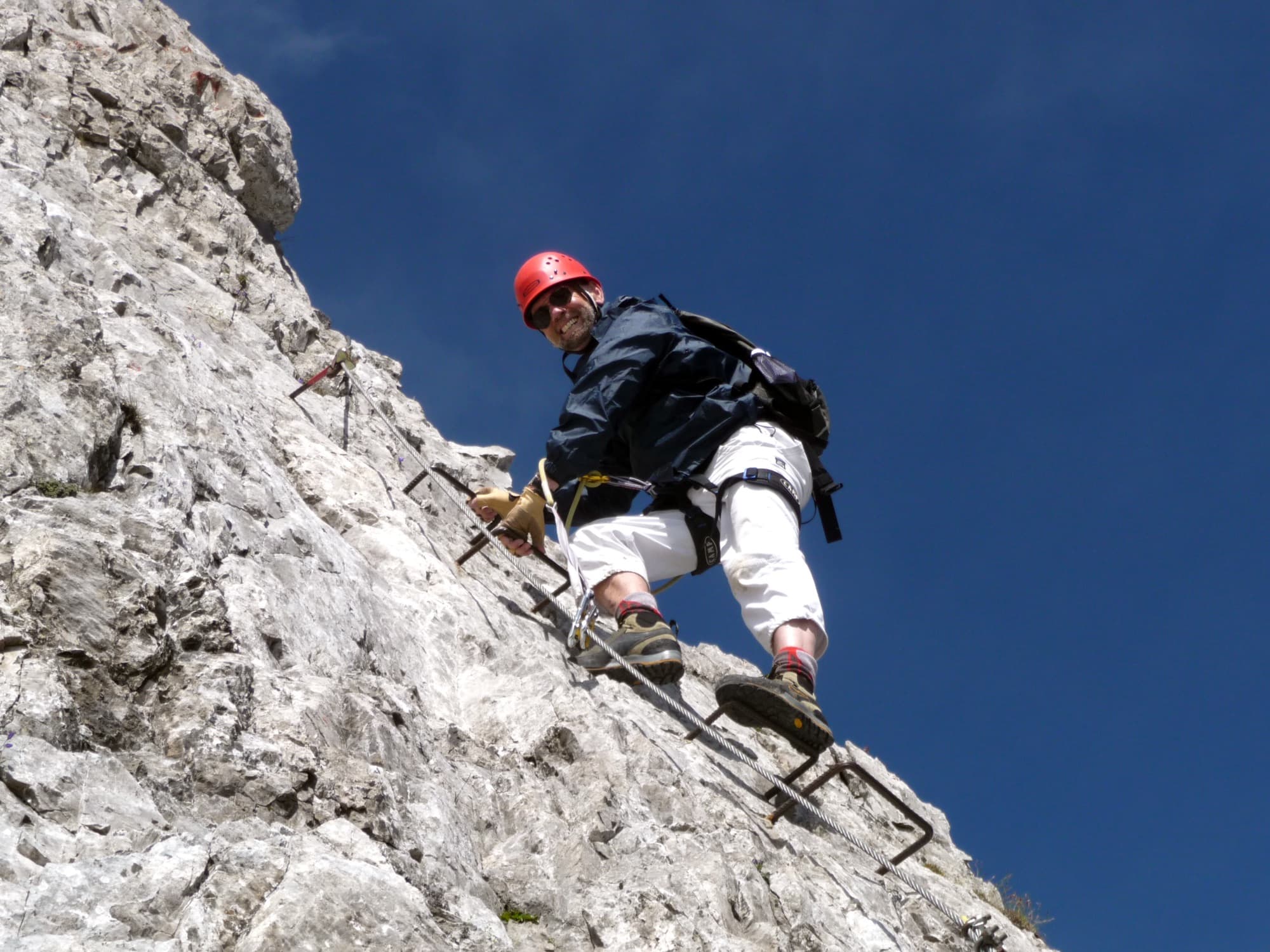 Paul Donders con casco rojo en una vía ferrata, bajo un cielo azul intenso
